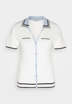 Cardigan blanco de manga corta con cuello azul, detalles en negro, dos bolsillos en el pecho con botones y cierre frontal abotonado.