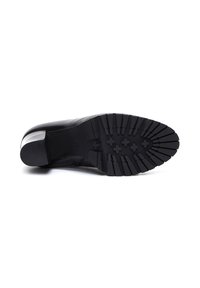 Chaussure en cuir noir vue du dessous, avec un motif de semelle et un petit talon carré, sur un fond blanc.
