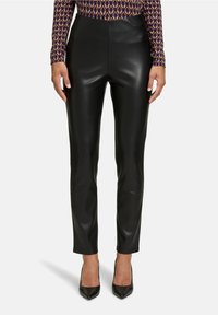 Pantalones de imitación de cuero negros con un diseño ajustado y cintura alta, combinados con unos tacones de punta negra. Textura suave sin patrones visibles.