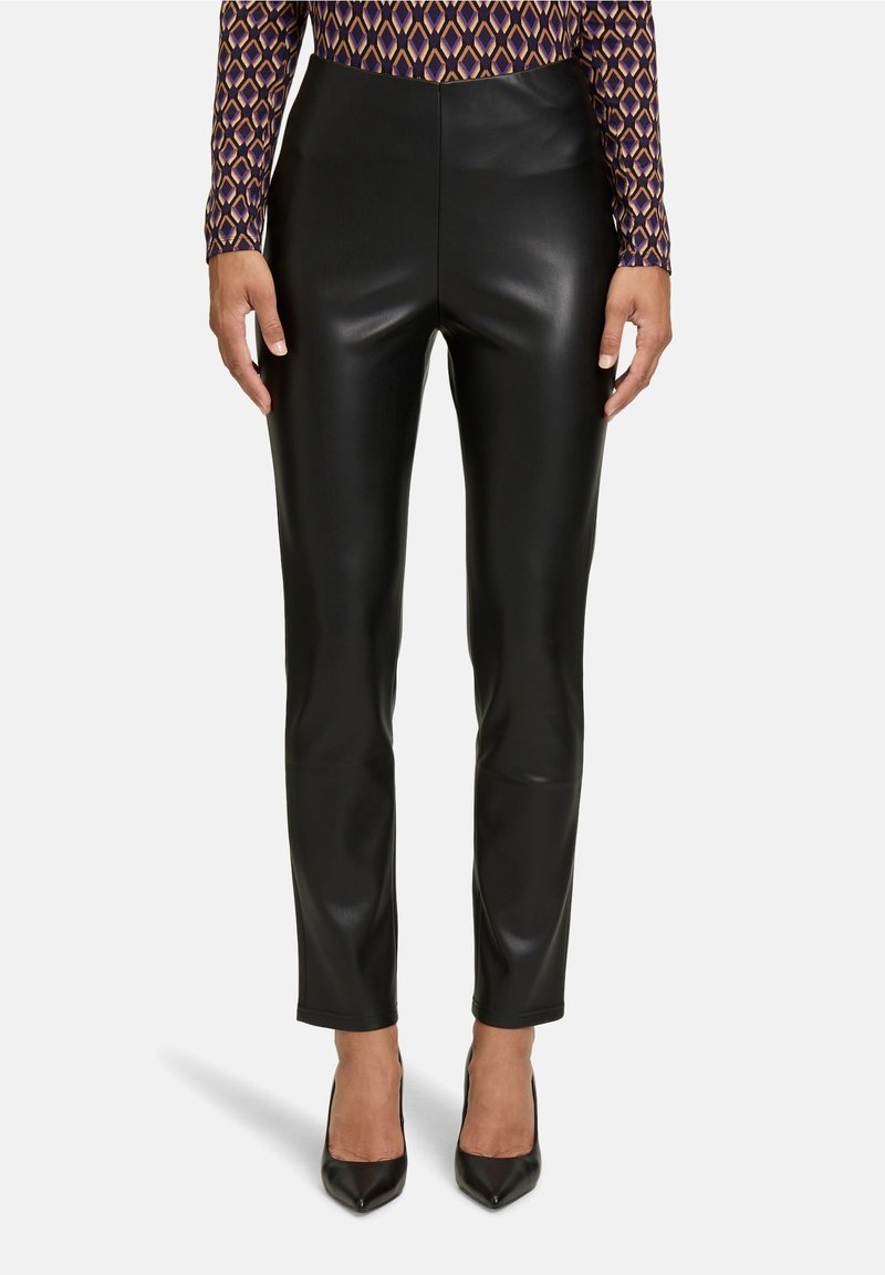 Pantalones de imitación de cuero negros con un diseño ajustado y cintura alta, combinados con unos tacones de punta negra. Textura suave sin patrones visibles.