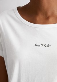 Witte katoenen t-shirt met ronde hals, korte mouwen en zwart geborduurd "Marc O'Polo" logo dichtbij de kraag. Zachte textuur.