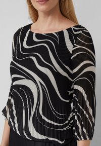 Schwarz-weiße Bluse mit Wellenmuster, gefältelter Textur und dreiviertelärmeln sowie rundem Ausschnitt.