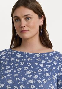 Blå blomstrete topp med båtutringning, med hvite blomstermønstre, jevn tekstur og avslappet passform.