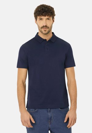 Marineblaues Poloshirt aus glattem Baumwollstoff, mit kurzen Ärmeln, einer geknöpften Knopfleiste und einem lockeren Schnitt, getragen mit blauen Jeans.