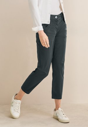 Mörkgrå, korta byxor med en mjuk textur och framfickor, bärs med vita sneakers med gröna detaljer.