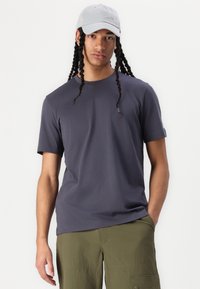 Pilkos trumpomis rankovėmis marškinėliai klasikinio silueto, pagaminti iš lygaus audinio, derinami su alyvinių spalvos krovinių šortais, turinčiais kelias kišenes ir laisvą dizainą.