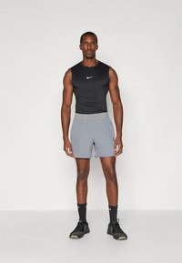 Mustad varrukateta sportlik top valge logoga; hallid lühikesed püksid elastse vöökoha jaos; mustad spordijalatsid; modell seisab neutraalses poosis.