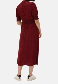 Abito midi rosso stampato con maniche a sbuffo corte, vita arricciata e zip sul retro. Abbinato a delle sneakers bianche con accento nero sul tacco.