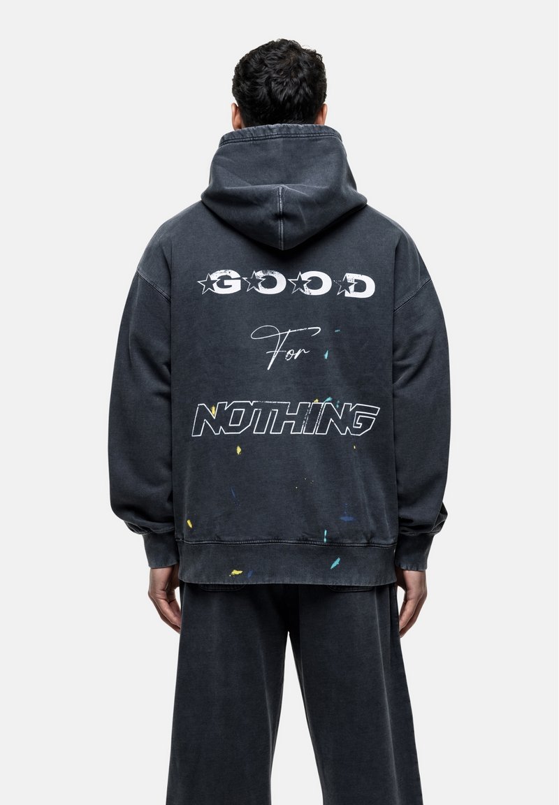 Oversized zwarte hoodie met witte tekst op de achterkant: "GOOD For NOTHING." Kleurige verfspetters aan de zoom.