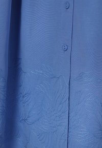 Tissu bleu avec fermeture à boutons et broderie florale subtile près du bord inférieur.