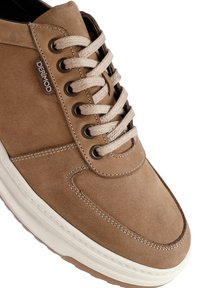 Zapato casual de ante marrón claro con cordones beige, ojales de metal oscuro, costuras visibles y suela de goma blanca, visto de cerca.