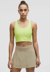Neon-grünes geripptes Croptop kombiniert mit einem beigen Sportrock. Glatter Stoff, taillierte Passform und elastischer Bund des Rocks.