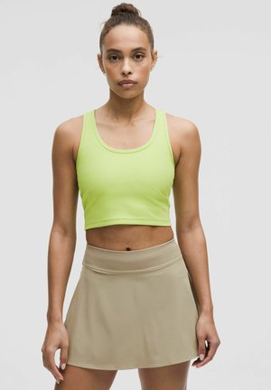 Neoonroheline ribikujuline crop top, mis on paaritatud beeži aktiivse skortiga. Sujuv kangas, sobiv disain ja elastsusega vöökoht skortil.