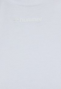 Tissu blanc texturé avec logo "hummel" embossé et symbole d'abeille centré près de l'encolure d'un vêtement.
