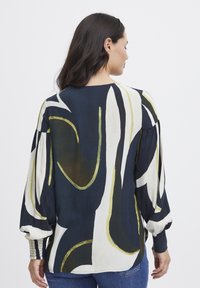 Blusa a fantasia con sfondo blu navy e disegni astratti in crema e verde. Maniche lunghe con dettagli arricciati ai polsini.