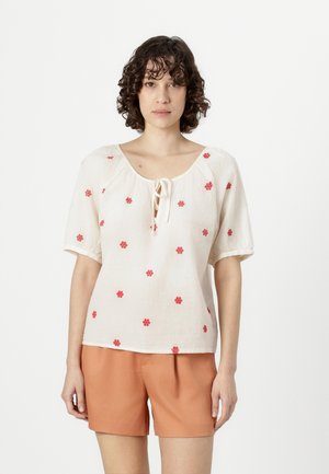 Bluză bej deschis, cu mâneci scurte, decorată cu broderie florală roșie și detaliu cu legare la gât. Asortată cu pantaloni scurți portocalii.