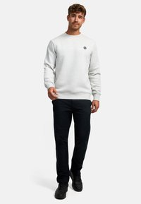 Sudadera gris con cuello redondo y puños de canalé, combinada con pantalones oscuros y zapatillas negras. Presenta un pequeño logo oscuro en el pecho.