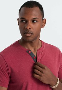 Camiseta roja de manga corta con cuello negro texturizado, que cuenta con dos botones rojos. La tela parece suave con un acabado jaspeado.