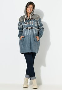 Blå mönstrad hoodie med snörning, framfickor och toggle-stängning. Kombinerad med mörka jeans och beige ankboots.