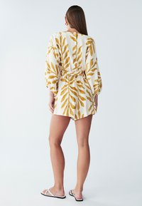 Rompertje met korte mouwen van lichtgewicht stof, met een witte achtergrond en gele bladpatronen, een getailleerde taille en knoopdetail aan de achterkant.