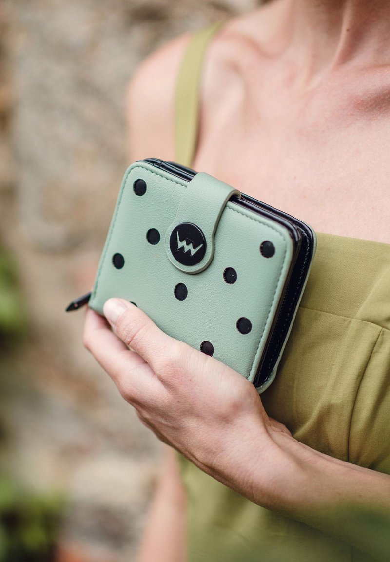 Mint green wallet with black polka dots, a black zipper and logo, and a snap closure. Smooth texture, compact rectangular shape.