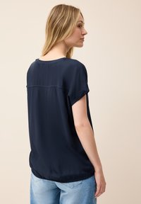 Blusa blu navy a maniche corte con scollo rotondo, vestibilità ampia e orlo arricciato, realizzata in un tessuto morbido e leggero.