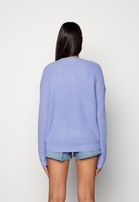 Lawendowy dziergany sweter o luźnym kroju, z okrągłym dekoltem, długimi rękawami i ściągaczem na dole, zestawiony z denimowymi szortami.