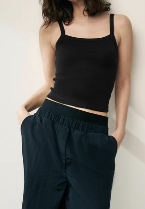 Sort fitted tank top med spaghetti-stropper, kombineret med løse mørkeblå bukser med elastisk talje og sidelommer.