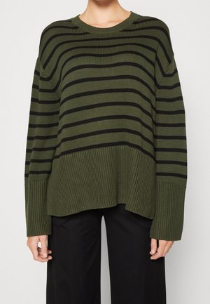 Person wearing an olive green sweater with black horizontal stripes and ribbed hem, paired with loose-fitting black pants.