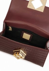 Borsa in pelle croccata di un profondo bordeaux con chiusura in hardware dorato. L'interno presenta un rivestimento scuro e una tasca con zip.