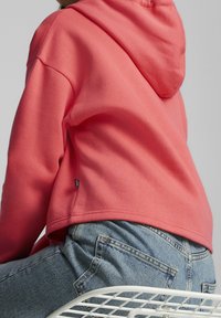 Felpa con cappuccio di colore rosa corallo, dal design cropped, texture morbida e fessure laterali. Abbinata a jeans in denim azzurri.