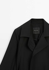 Trench-coat noir à larges revers, présenté sur fond blanc, avec une étiquette intérieure visible portant l'inscription "Massimo Dutti".