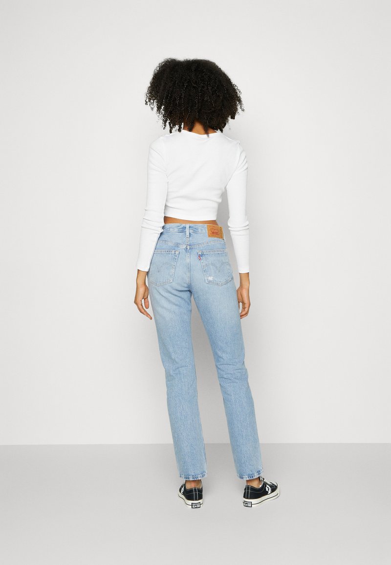 Jeans de denim de lavado claro con un ajuste de pierna recta, bolsillos traseros y un parche de cuero con marca en la cintura trasera. Combinados con zapatillas negras.