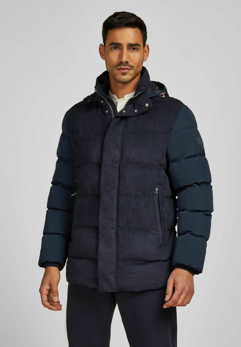 Dunkelblaues Steppjacke mit einer glatten, weichen Textur. Verfügt über einen Reißverschluss auf der Vorderseite, seitliche Taschen und eine abnehmbare Kapuze. Gestepptes Design.