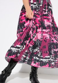 Abito plissettato in un vivace rosa, con un motivo astratto in bianco e nero. Presenta una silhouette fluida, tessuto texturizzato e si abbina a stivali neri alti fino al ginocchio.