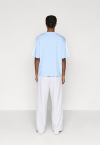 Világoskék rövid ujjú pamut póló, fehér oldalsávokkal. Világosszürke, bőszárú nadrággal párosítva. Egyszerű és lazán illeszkedő fazon.