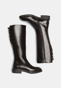 Bottes en cuir marron foncé, arrivant au genou, avec une finition lisse, une fermeture éclair sur le côté et des accents de boutons à l'arrière pour un ajustement réglable.