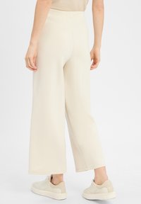 Wijdvallende, crème-kleurige broeken met een gladde, zachte textuur. Voorzien van een hoge tailleband en subtiele stikdetails. Combinatie met lichte sneakers.