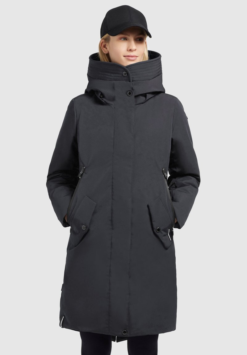 Black long coat with a high collar, side pockets, and a button closure. Made of smooth, water-resistant fabric. Accompanied by a black cap.