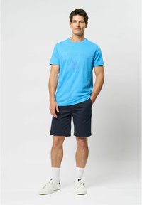 Lyseblå T-shirt med kort ærme, med teksten "U.S. Polo Assn." og logo, parret med marineblå shorts og hvide sneakers. Lavet af bomuldsstof, afslappet pasform.
