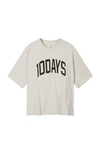 Jasnoszara, oversize'owa koszulka z krótkim rękawem z wyraźnym czarnym nadrukiem z napisem "100DAYS" na przodzie. Gładka tekstura.