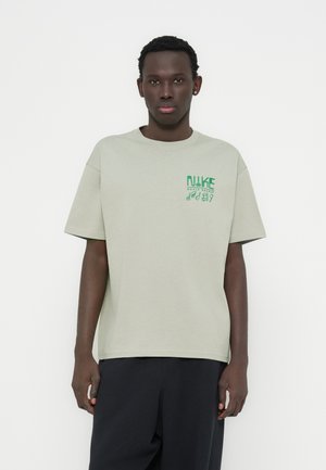 Camiseta de algodón verde claro con mangas cortas, que presenta un logo en verde oscuro, corte relajado y cuello redondo.