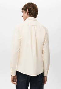 Camicia a maniche lunghe beige chiaro con collo con bottoni, plissettatura sul retro e polsini con un solo bottone, abbinata a jeans denim scuro.