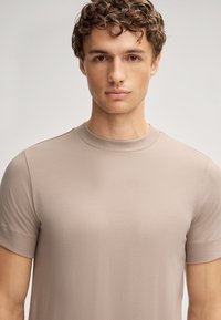 T-shirt en coton beige clair à manches courtes avec un col rond, texture lisse et design minimaliste. Pas de logos ni de décorations visibles.