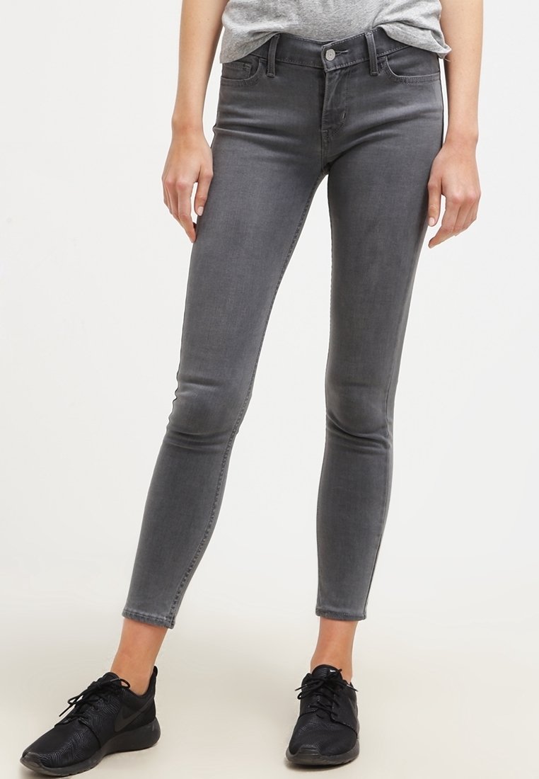 Jeans ajustados grises con una textura suave, que presentan un cierre de botón en la parte delantera y un ligero desvanecimiento. Combinados con zapatillas deportivas negras.