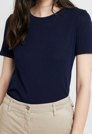 Granatowy t-shirt z krótkim rękawem wykonany z miękkiego materiału, z okrągłym dekoltem. Dobry do jasnobeżowych spodni z przodu ozdobionych guzikami.