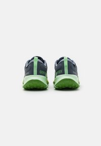Para ciemnoszarych i zielonych butów biegowych Gore-Tex ukazane z tyłu, podkreślające zielone uchwyty i teksturowane zielone podeszwy.