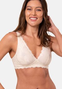 Koronkowy biustonosz w odcieniu kremowym z głębokim dekoltem, szerokimi ramiączkami i miękką teksturą. Delikatne detale koronki podkreślają cały projekt.