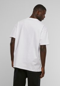 Hvid bomulds t-shirt med korte ærmer, rund halsudskæring, løs pasform og en glat tekstur. Bagsiden viser en let buet kant.