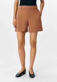 Shorts marron ajustés en tissu lisse, dotés de poches latérales et d'une coupe droite, associés à des ballerines noires.